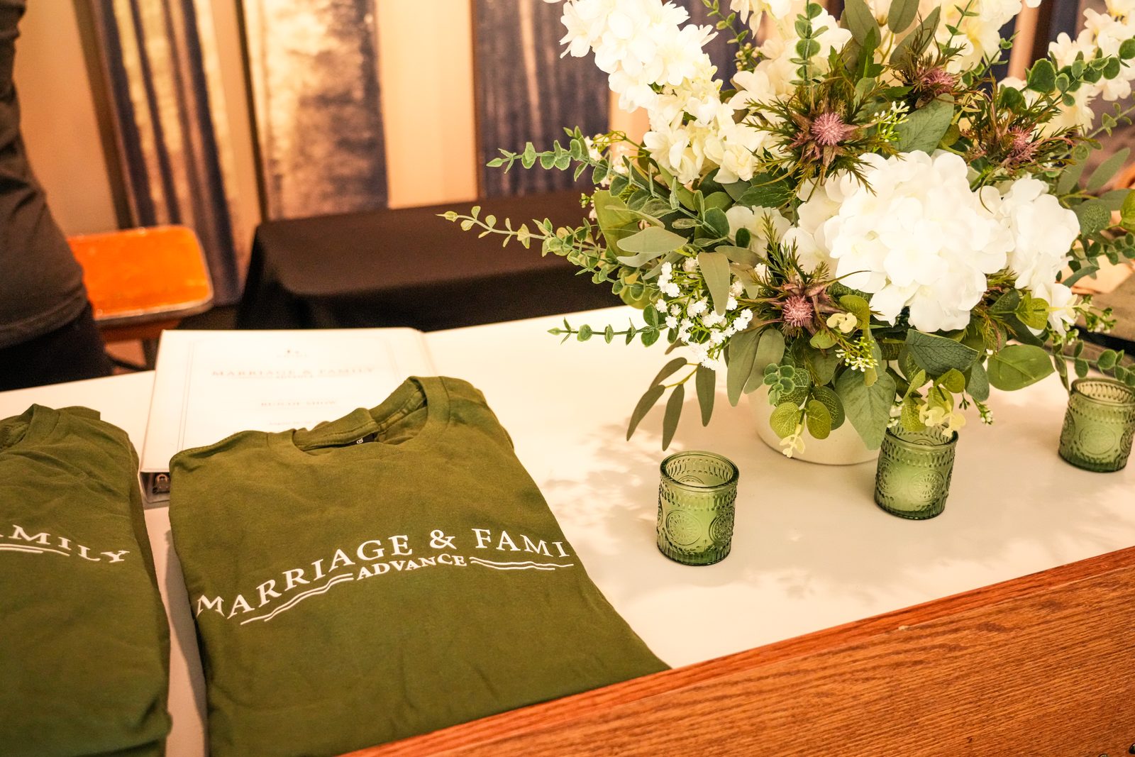 The welcome table on arrival evening at the 2026 Advance, with folded Marriage and Family Advance shirts, a binder and white flowers