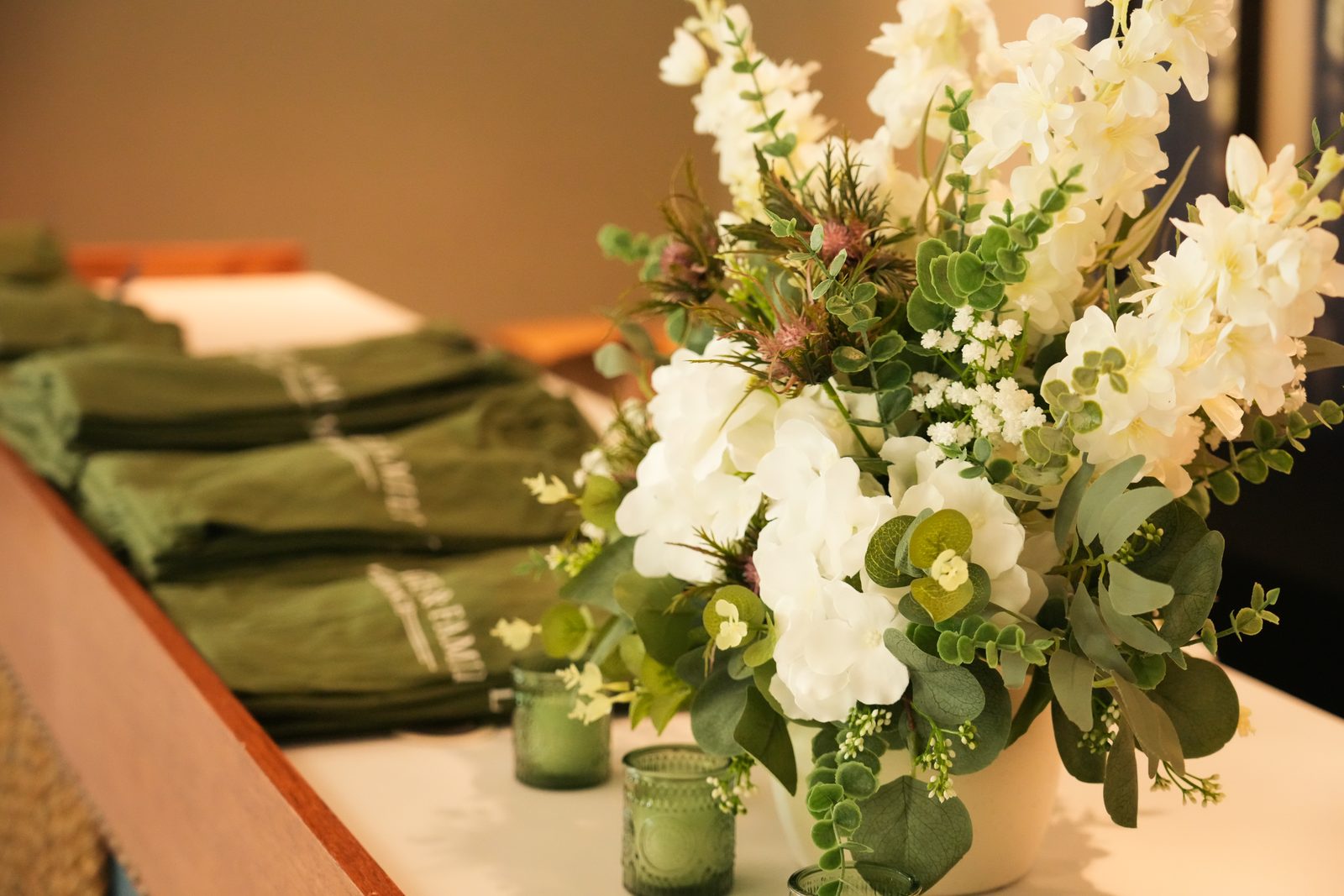 Stacks of folded green Marriage and Family Advance shirts beside white flowers and green glass candle holders