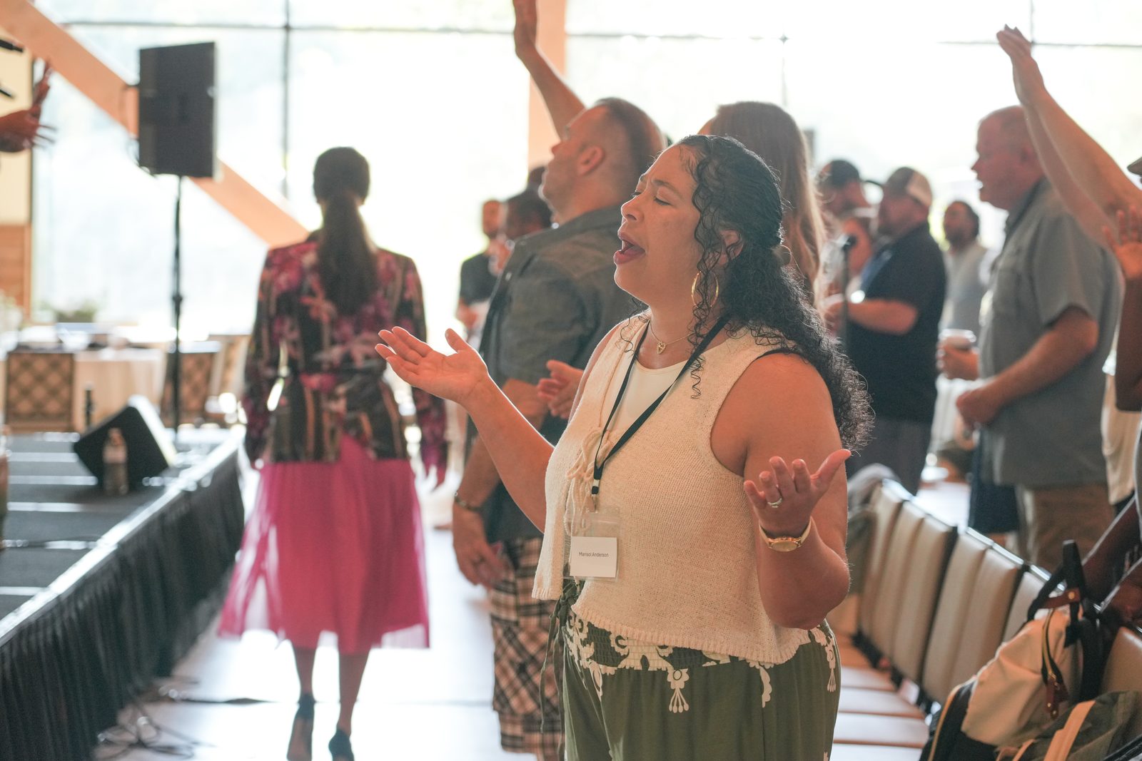 A woman worshipping with open hands during a session, couples standing around her with arms raised