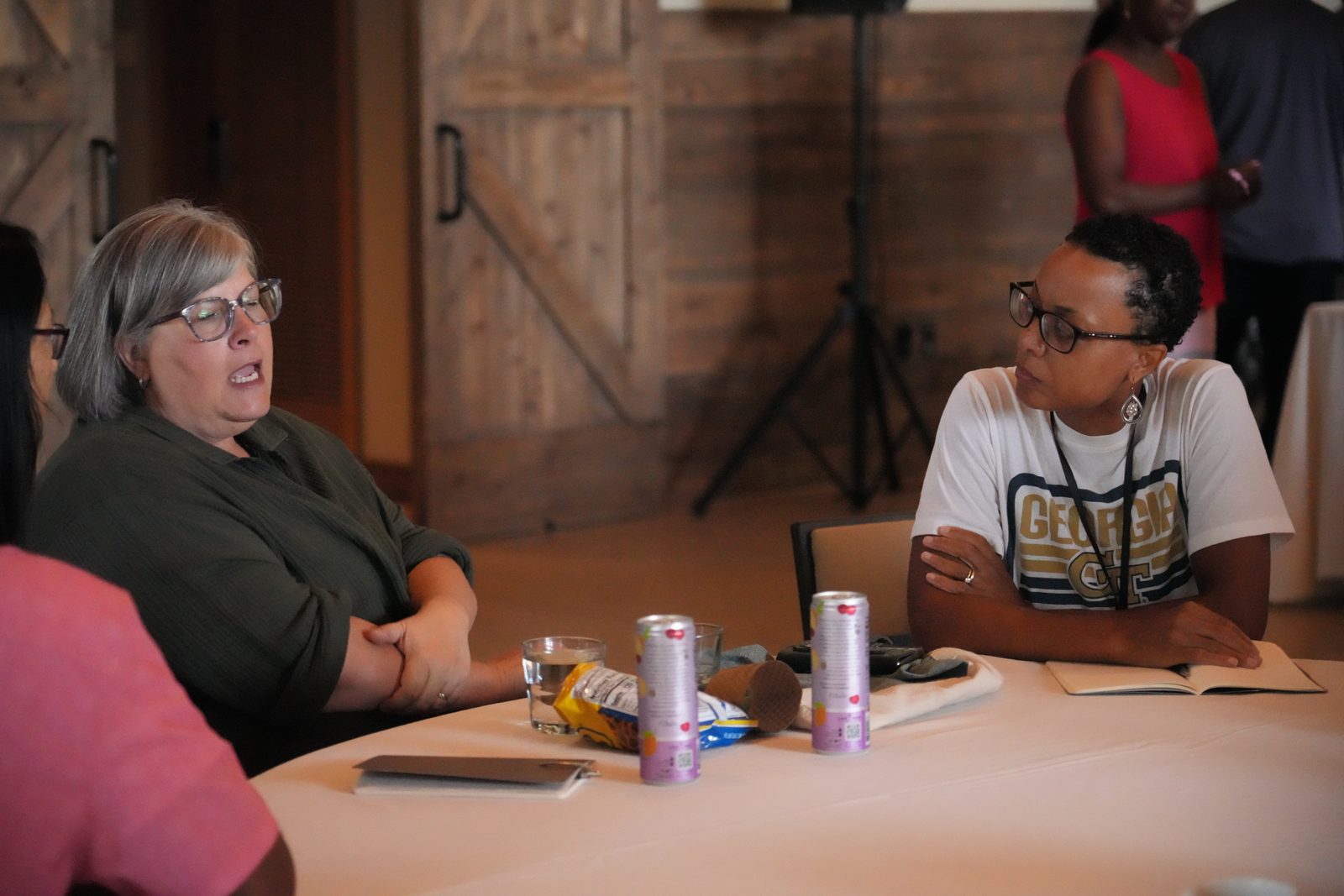 Two women talking across a round table during a session, one with her journal open