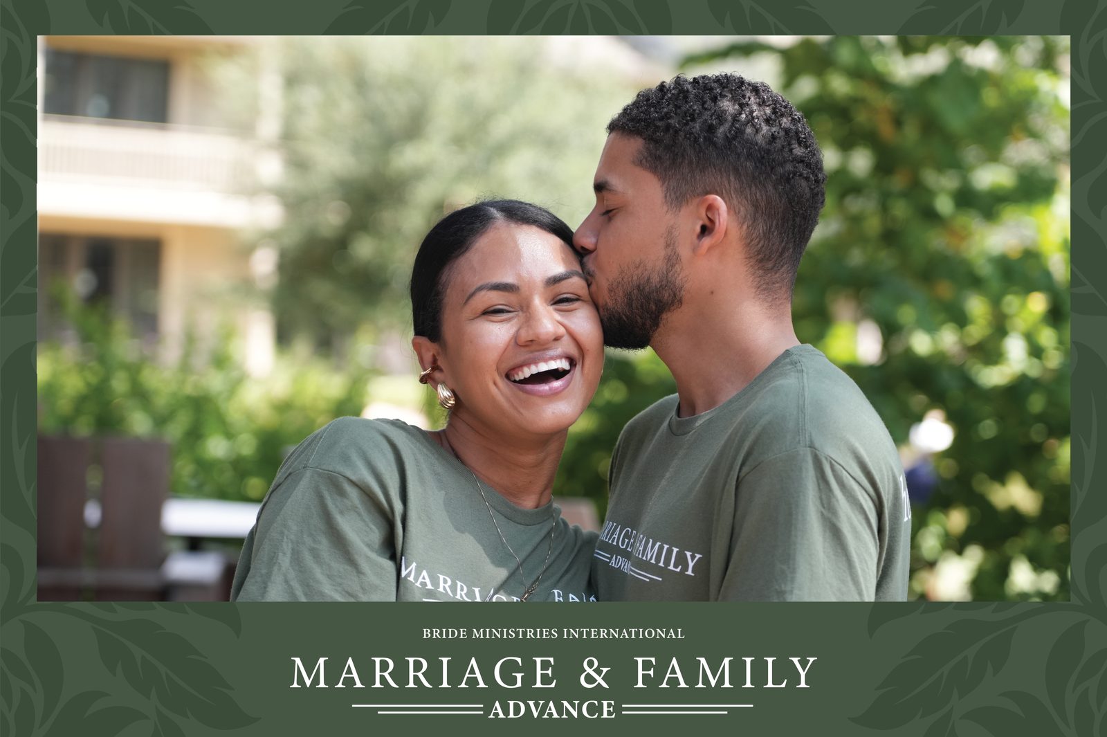 A husband kissing his wife on the temple as she laughs, both in Marriage and Family Advance shirts, in their portrait
